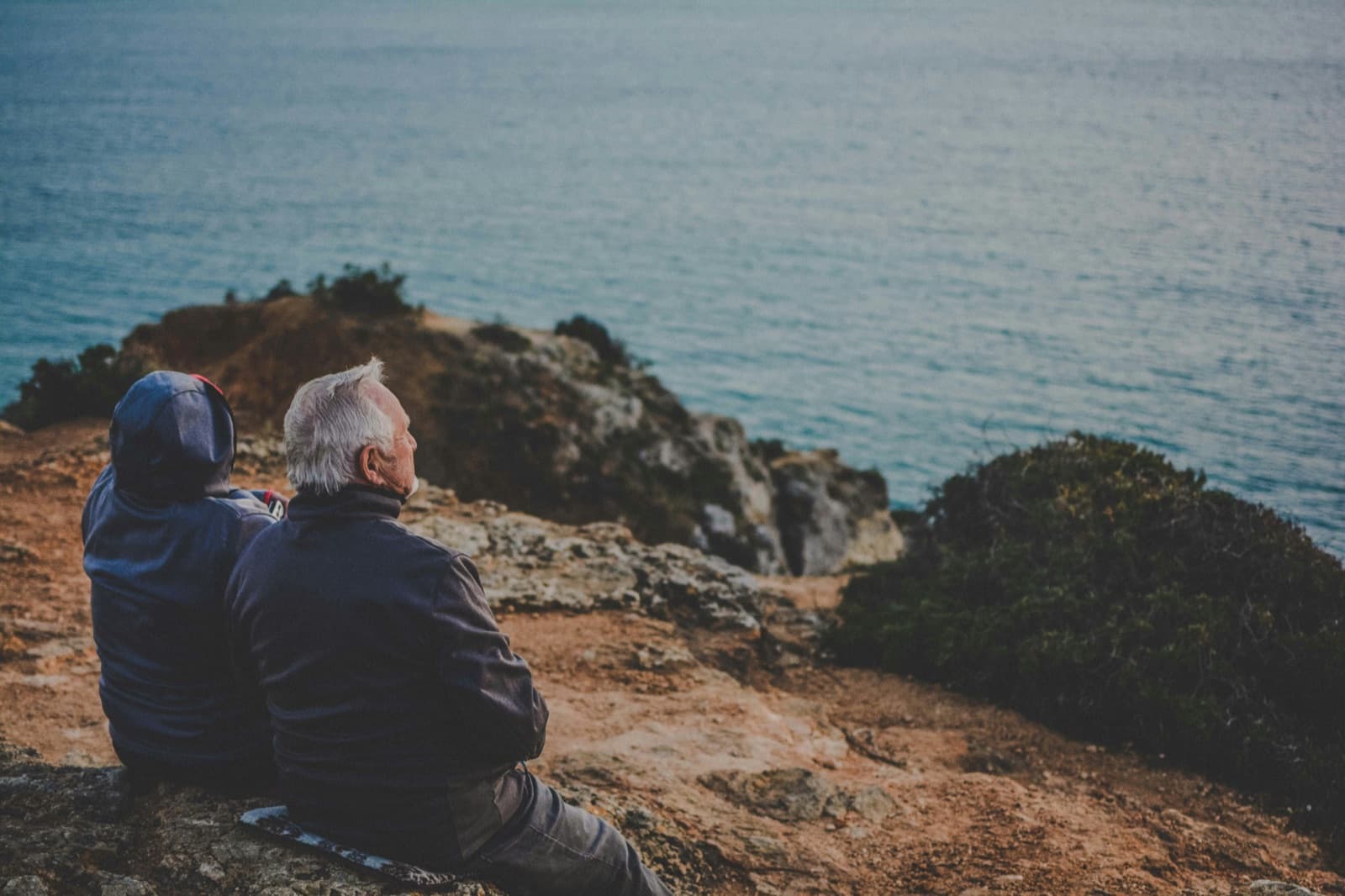 Two people sitting on a rock looking out over the water